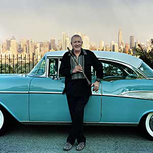 Paquito D'Rivera standing in front of blue car and Manhattan Skyline