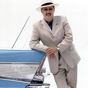 Paquito D'Rivera with panama hat leaning against blue car